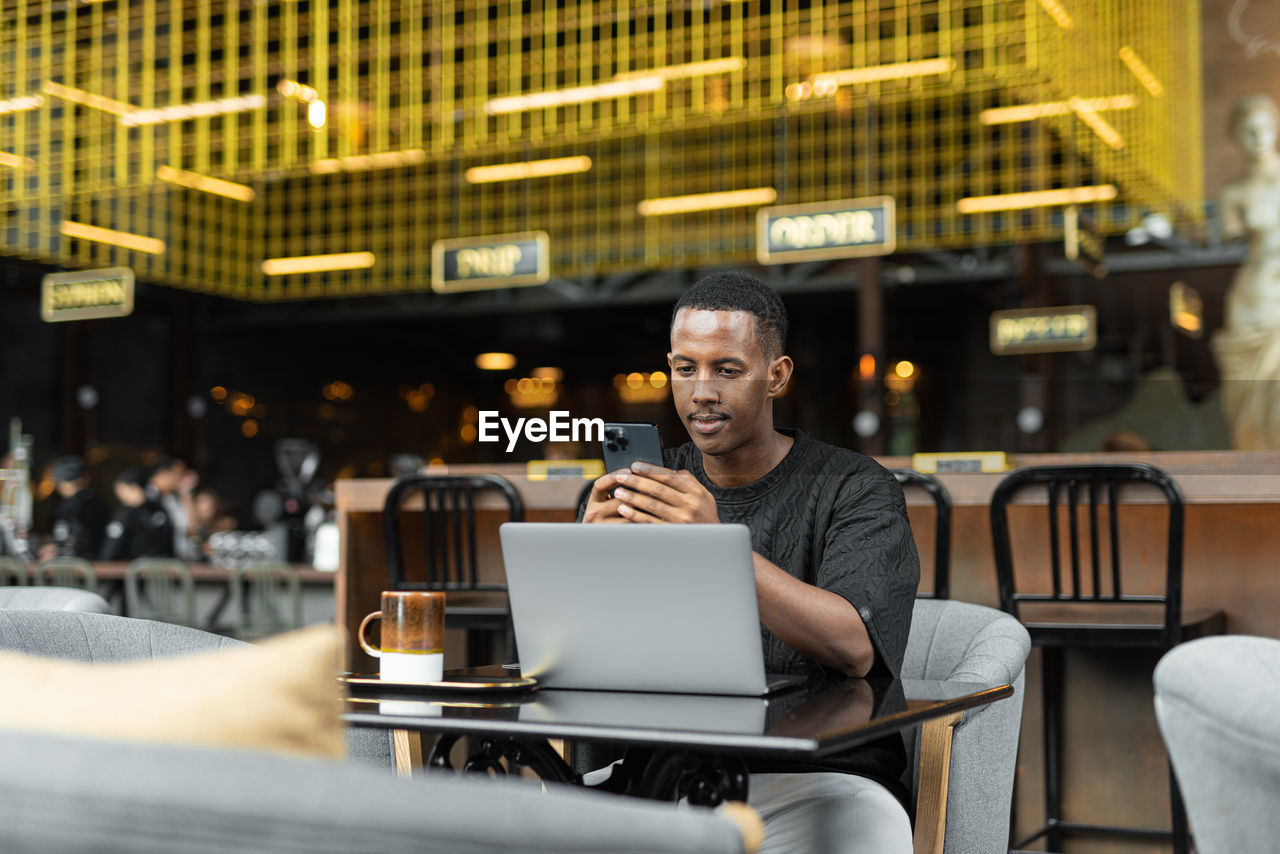 young woman using mobile phone while sitting at cafe