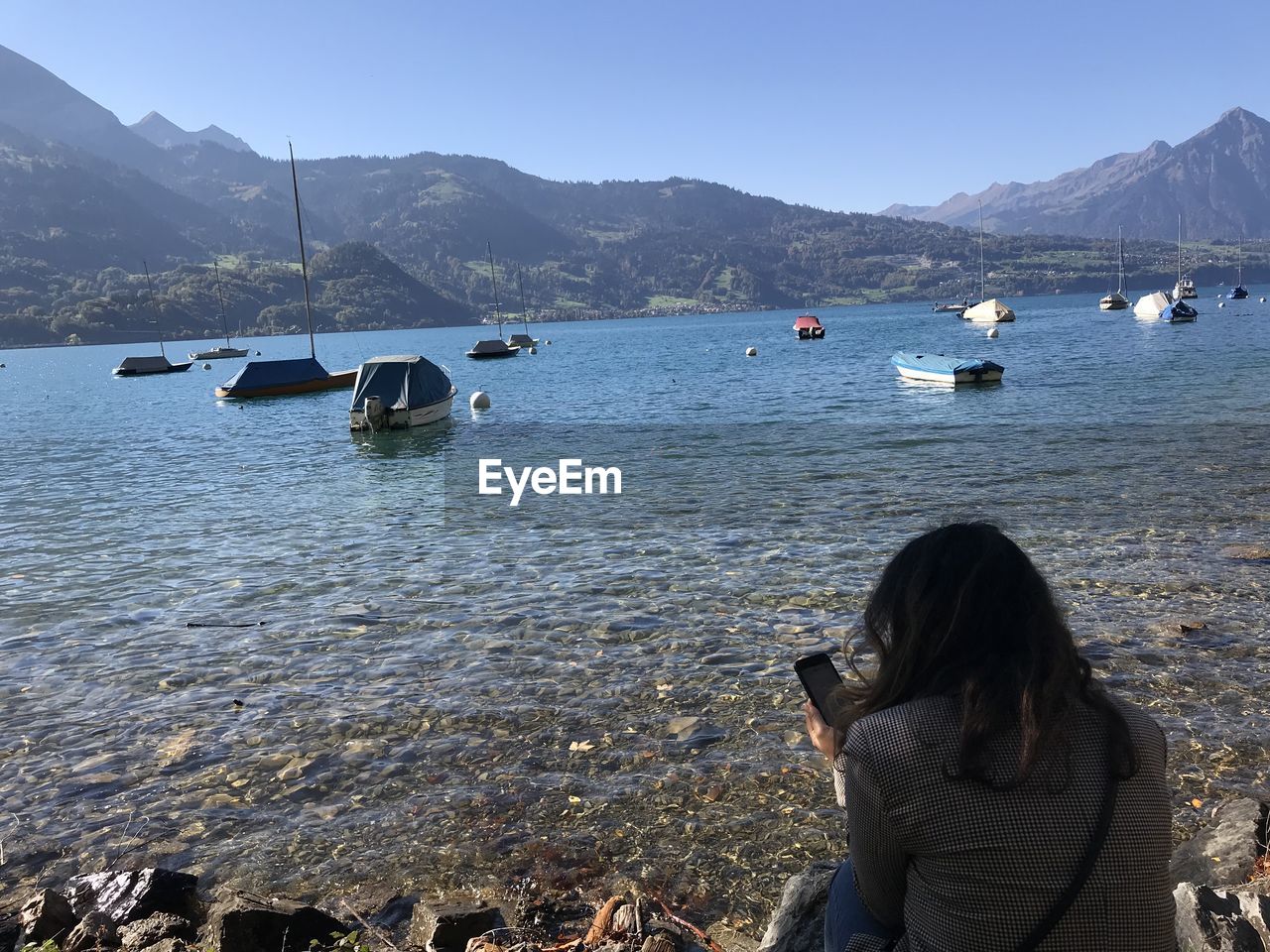 REAR VIEW OF WOMAN ON SEA AGAINST MOUNTAINS