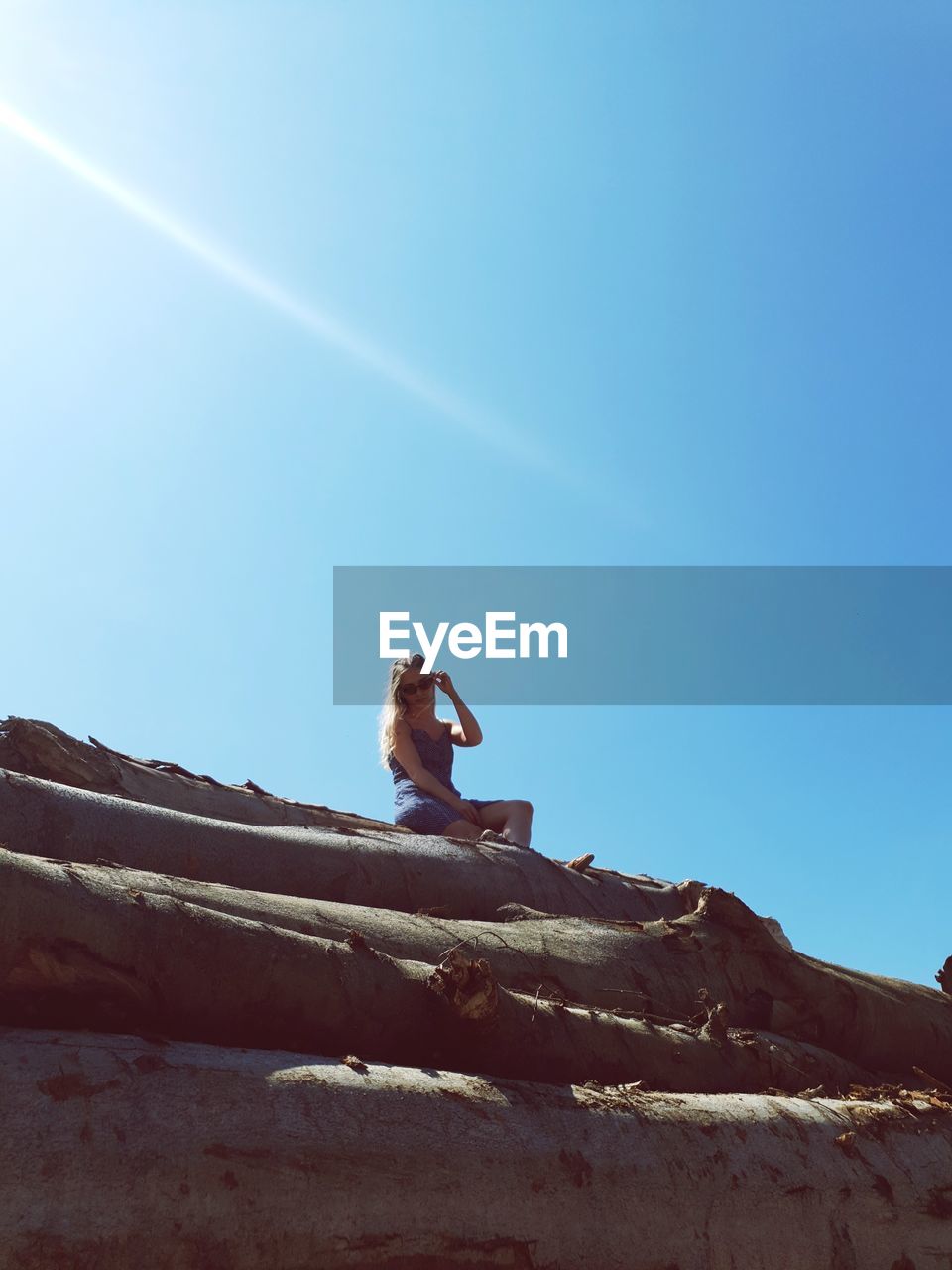 Low angle view of woman sitting on wood against clear sky
