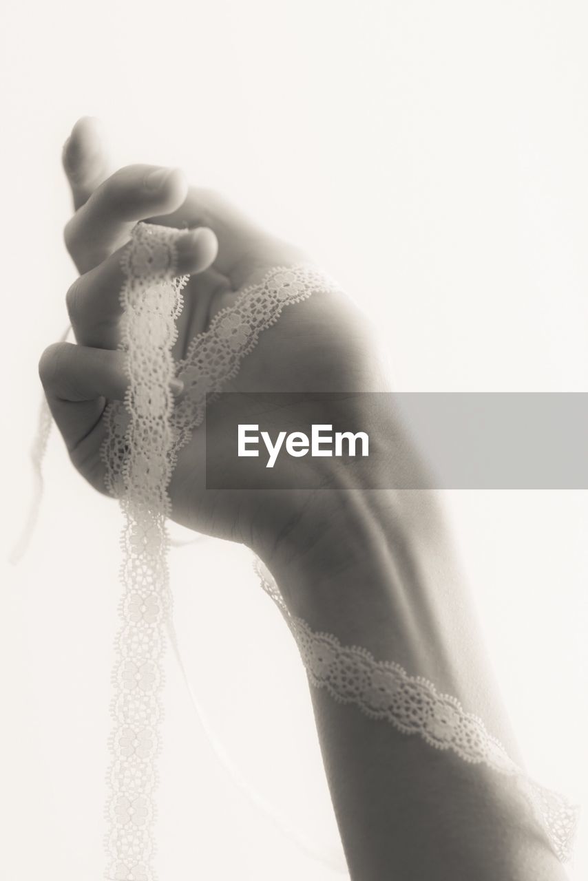 Close-up of hand holding lace over white background