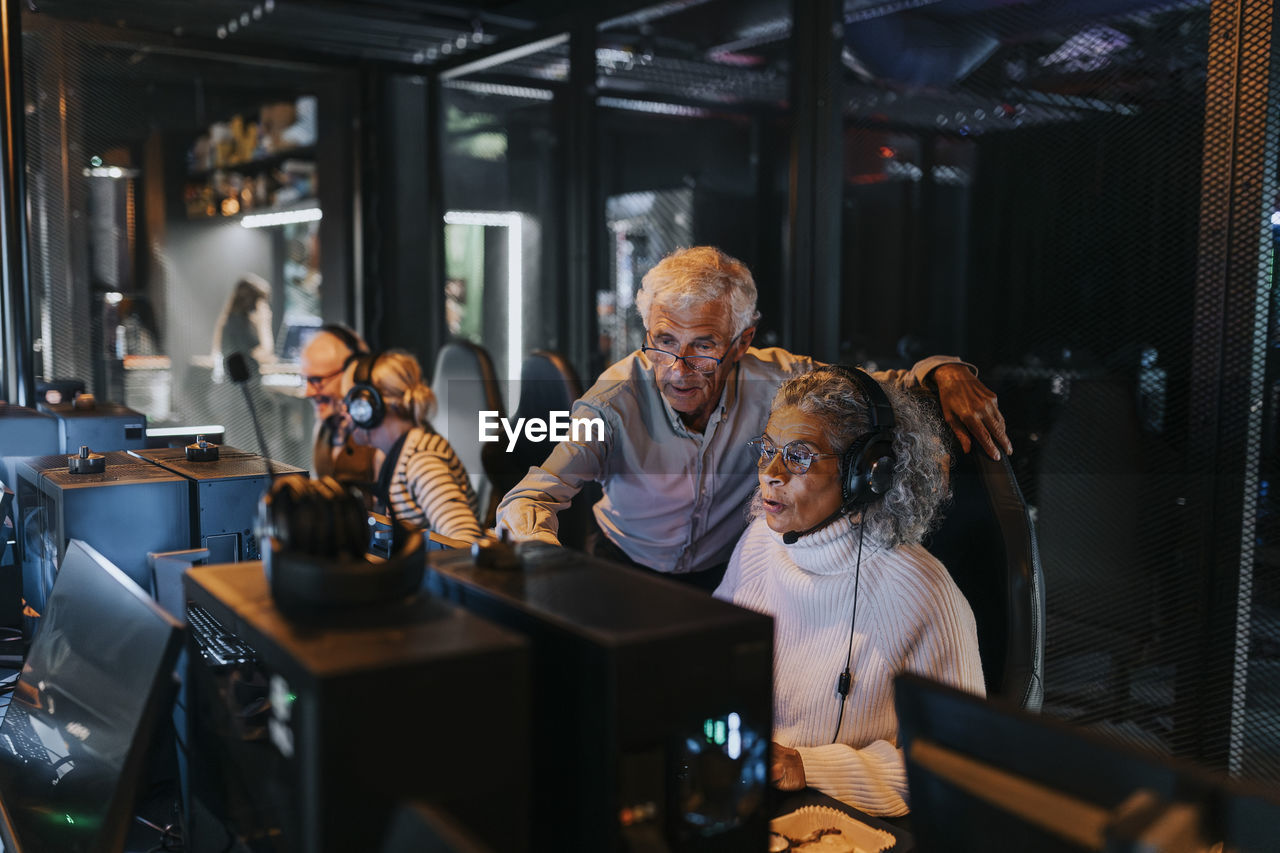 Heterosexual couple playing video game by male and female friends in gaming center during weekend