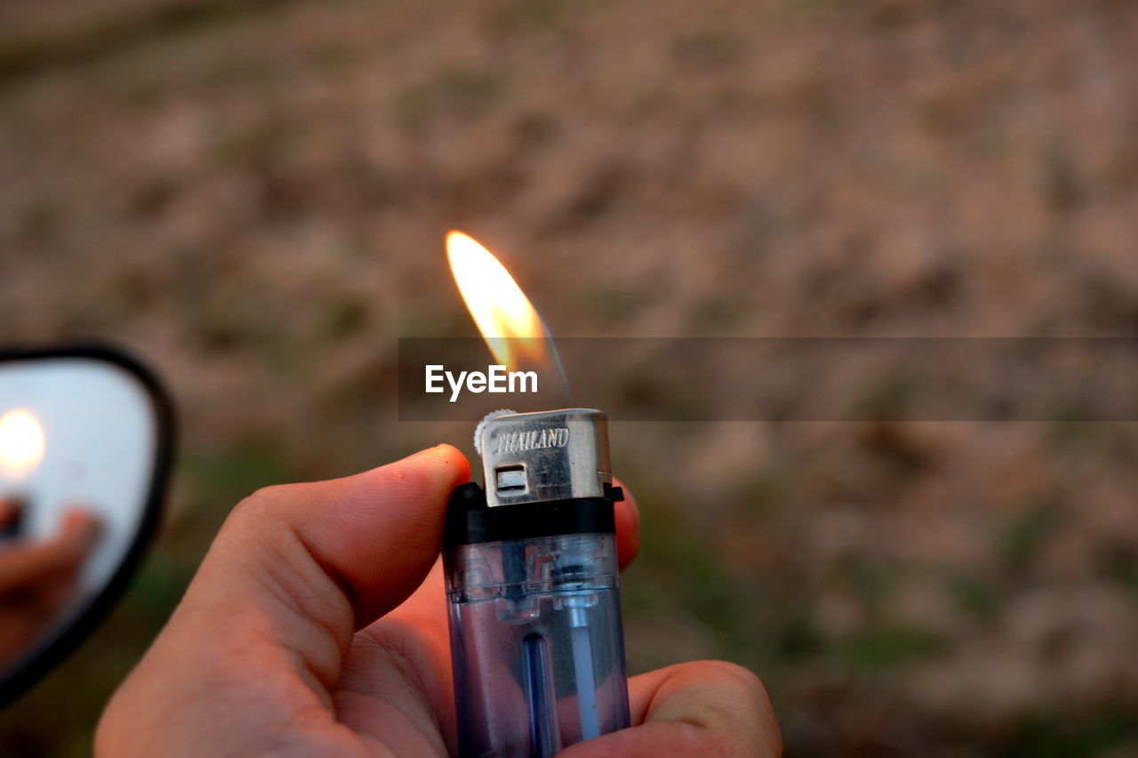 Close-up of hand holding burning cigarette lighter outdoors