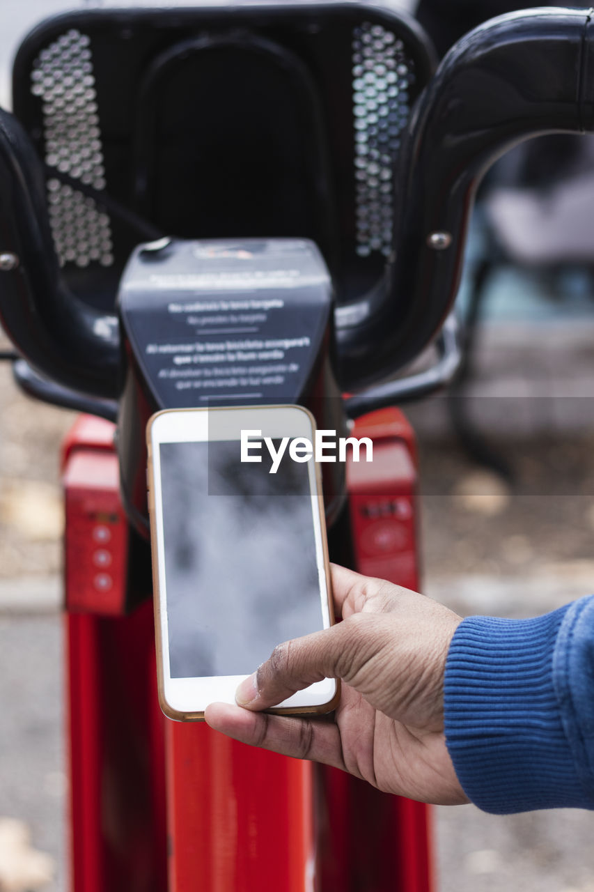 Hand of man renting bicycle through smart phone at parking station