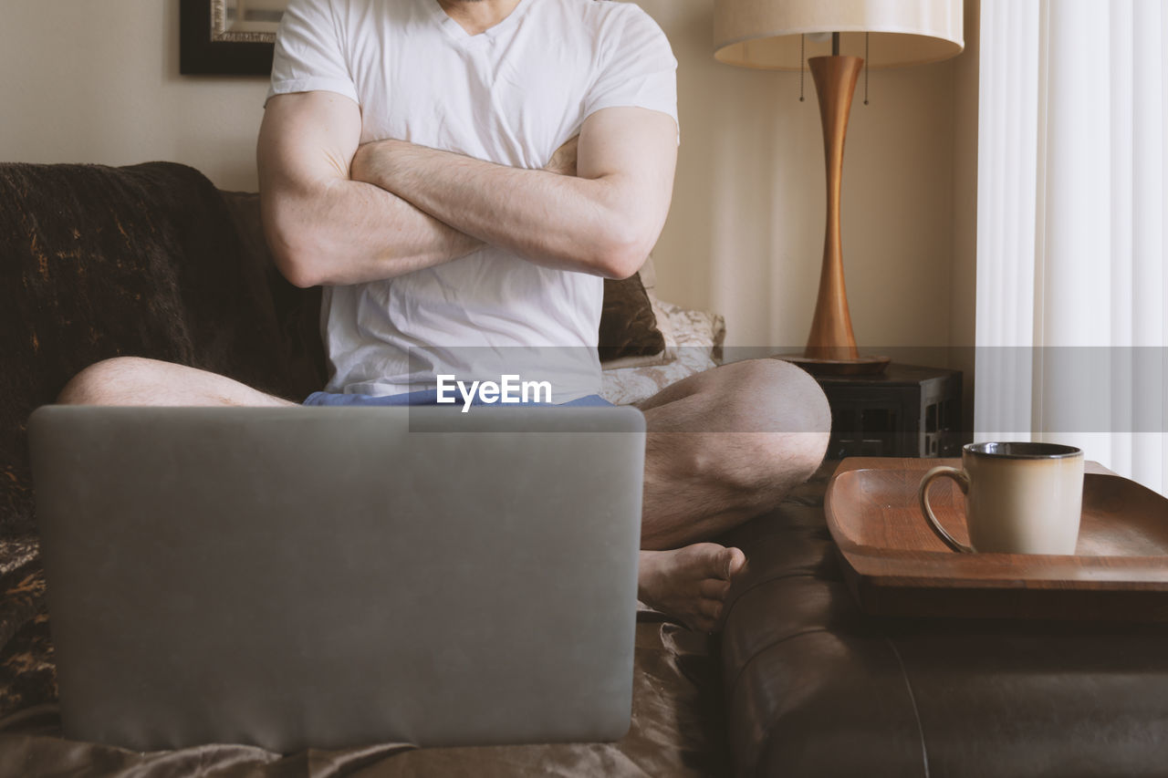 Male torso arms crossed watching laptop computer screen in morning.