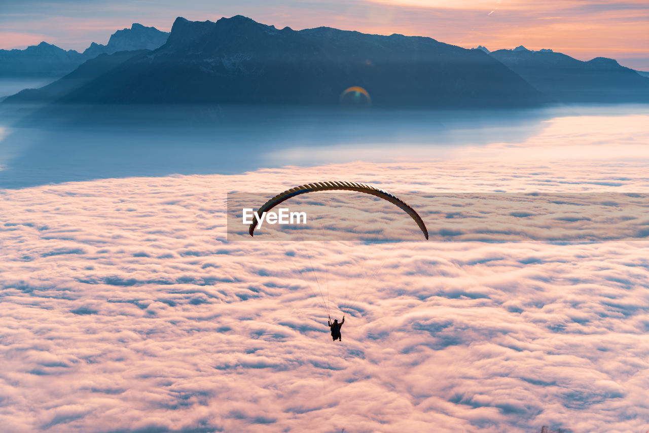 Silhouette of person paragliding over cloudscape