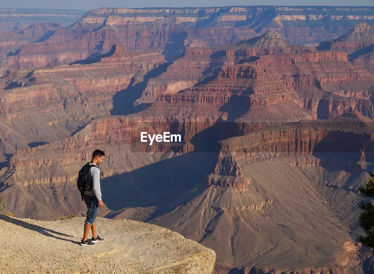 FULL LENGTH OF MAN STANDING ON ROCK AT MOUNTAIN