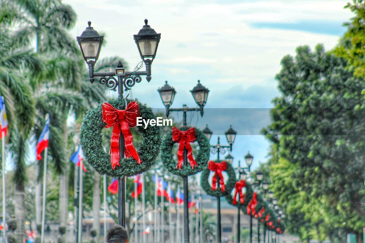 Low angle view of wreaths hanging on street lights against cloudy sky