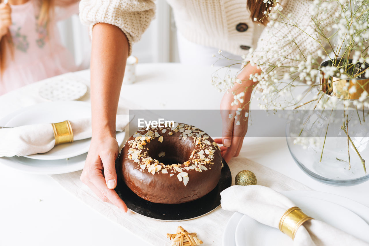 Young woman holding in hands large round chocolate almond cake on table with new year serving