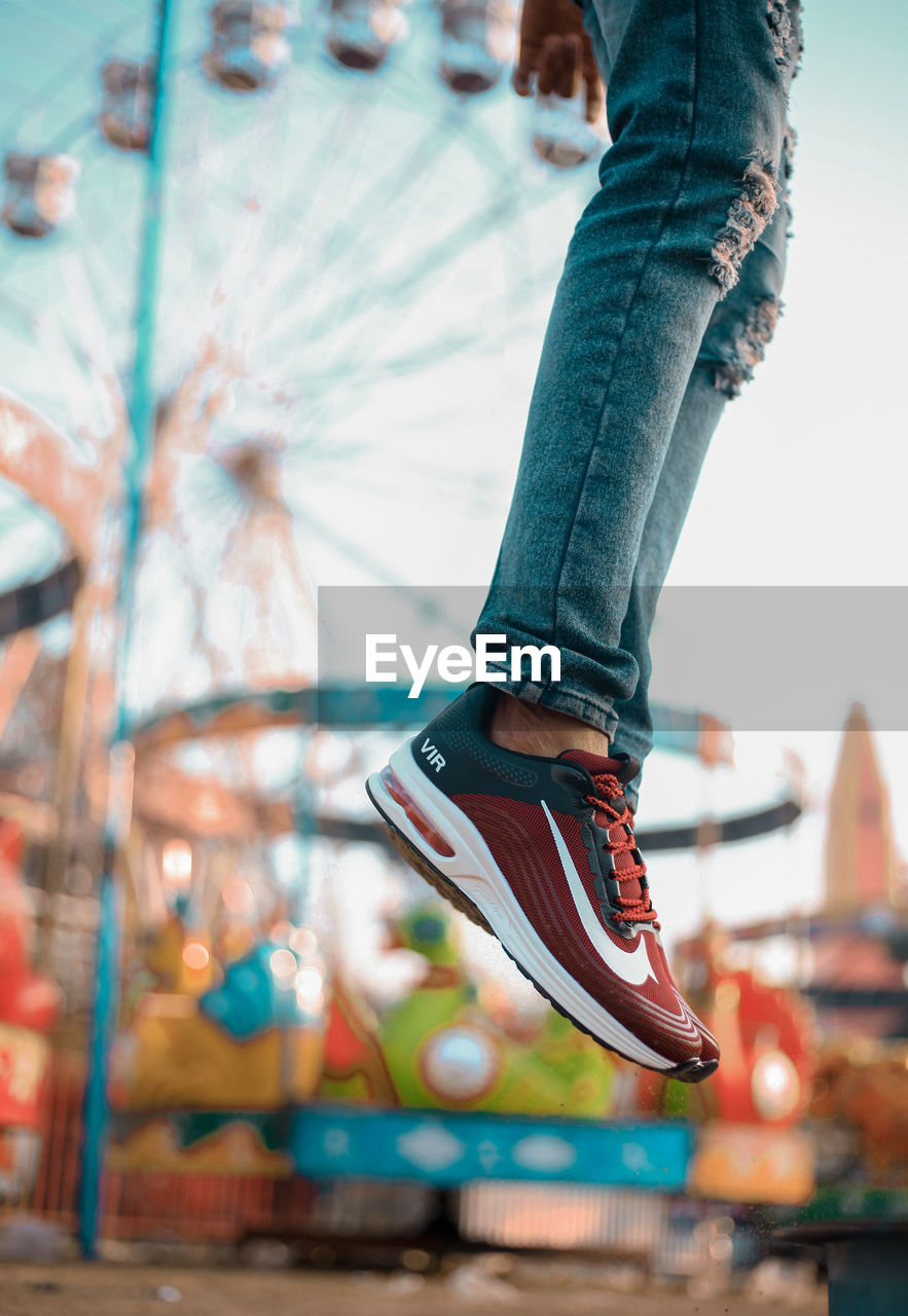 LOW SECTION OF PERSON WITH CAROUSEL IN AMUSEMENT PARK