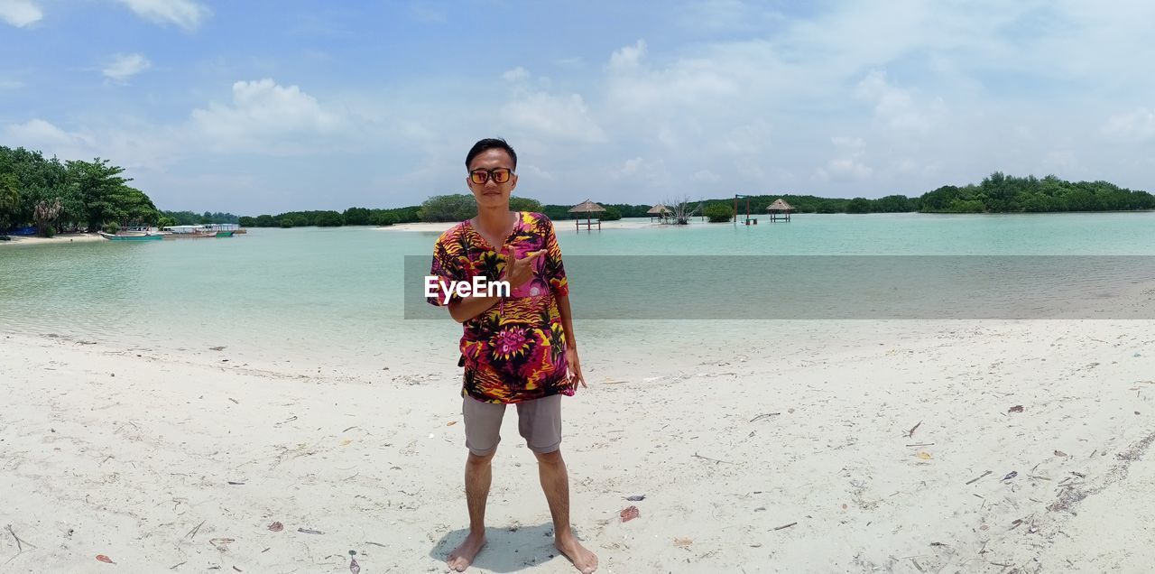 Portrait of man standing at beach against sky