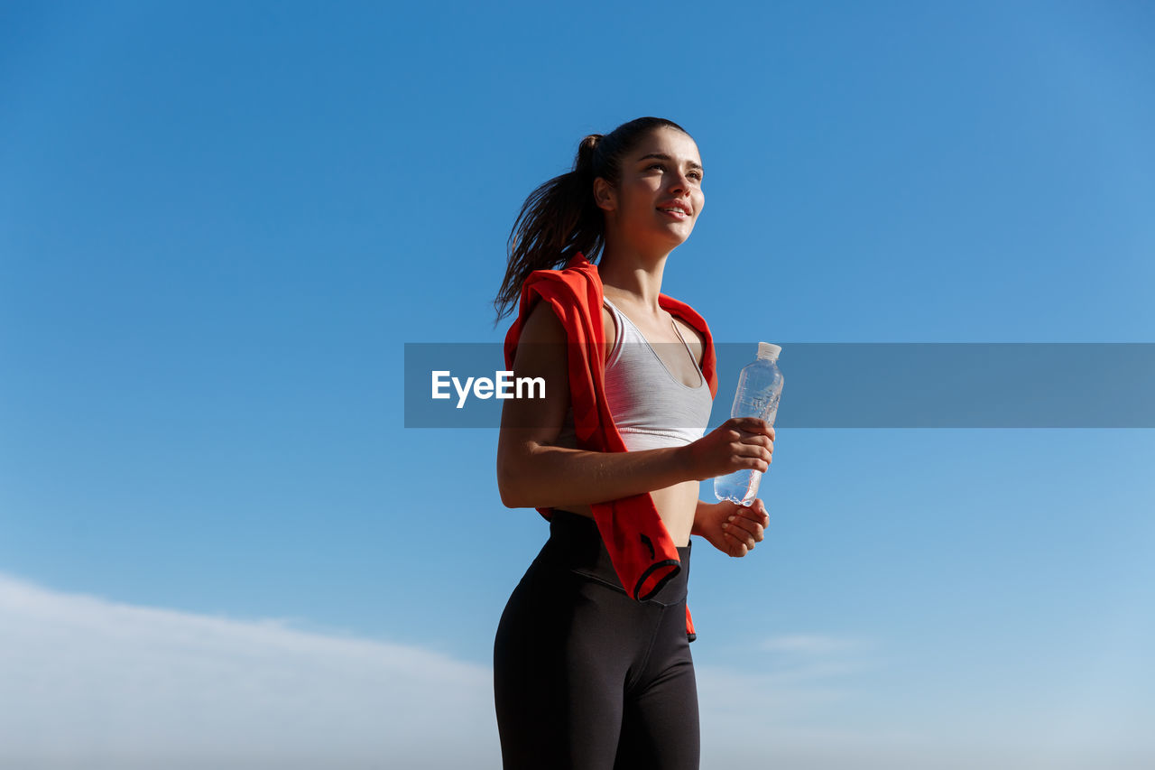 Low angle view of woman jogging against clear sky