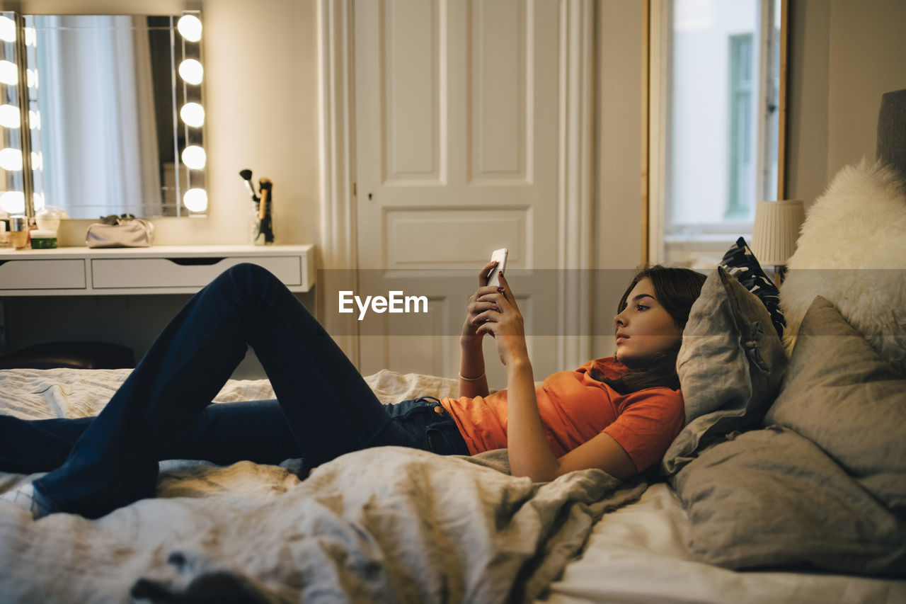 Girl using mobile phone while lying on bed at home