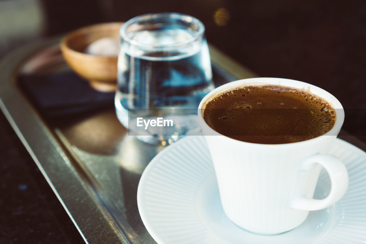 Turkish mocha coffee on metal tray with water in small glass and small cookie in wooden bowl.