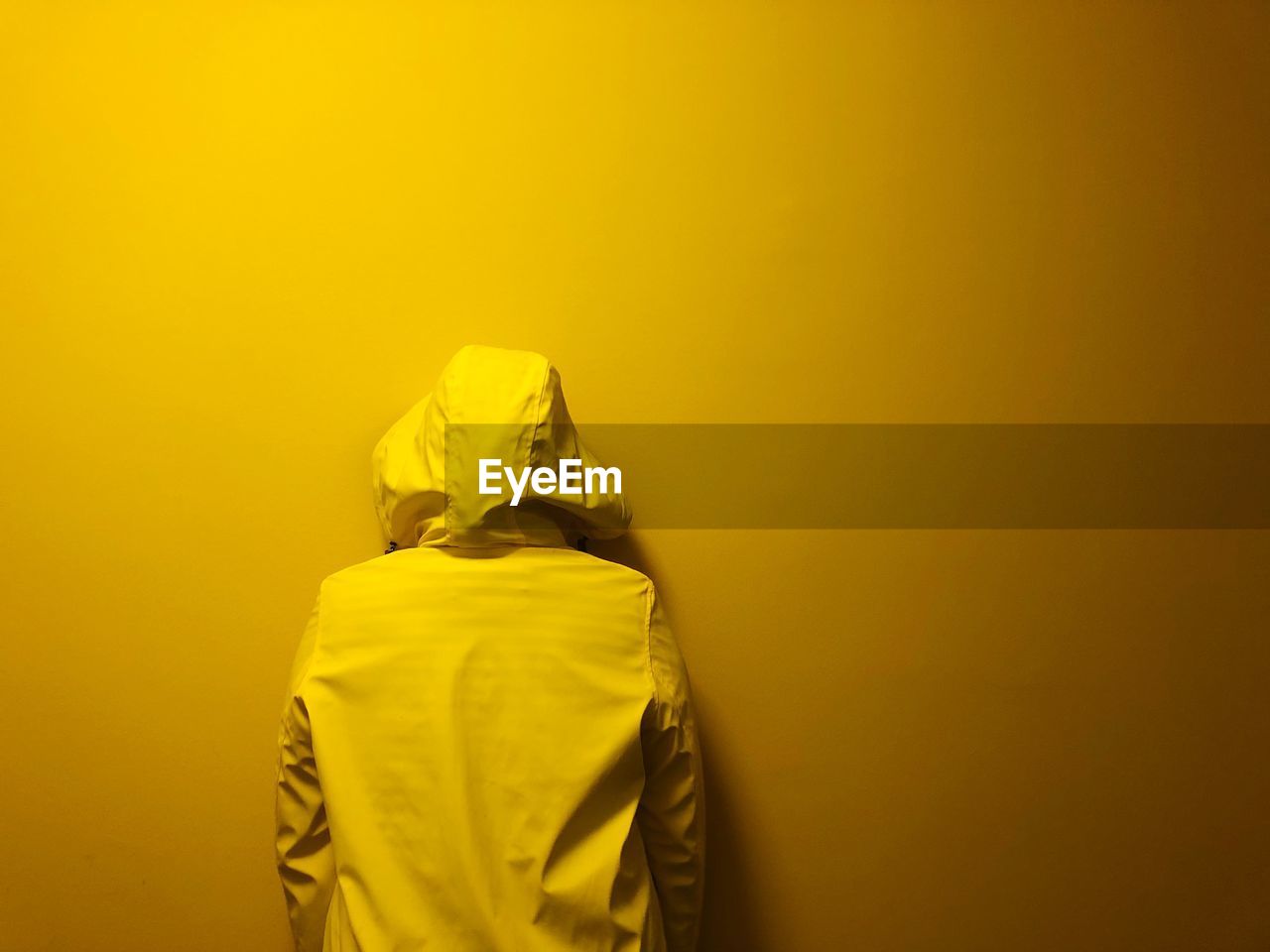 Rear view of person wearing hooded shirt standing against yellow wall