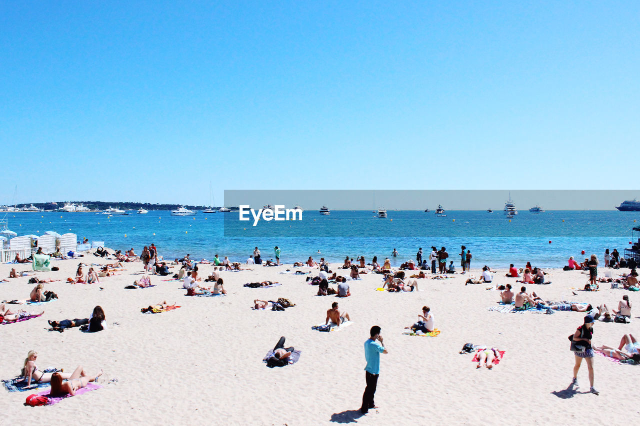 Group of people on beach against clear blue sky