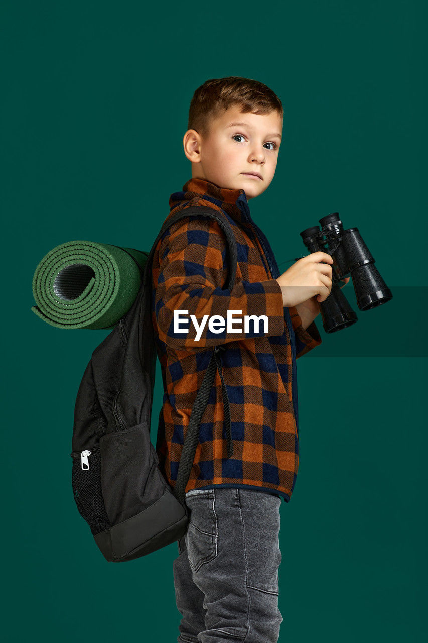portrait of boy holding camera against blue background