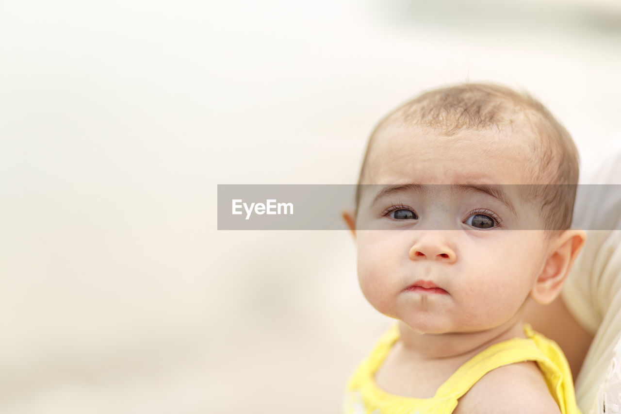 Infant baby with bright eyes isolated with shallow depth of field against light colored background