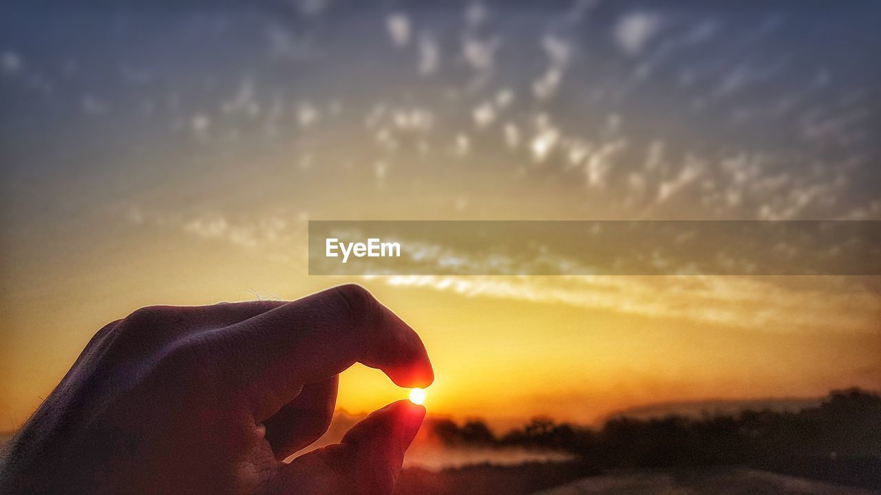 Close-up of silhouette hand holding sun against sky during sunset