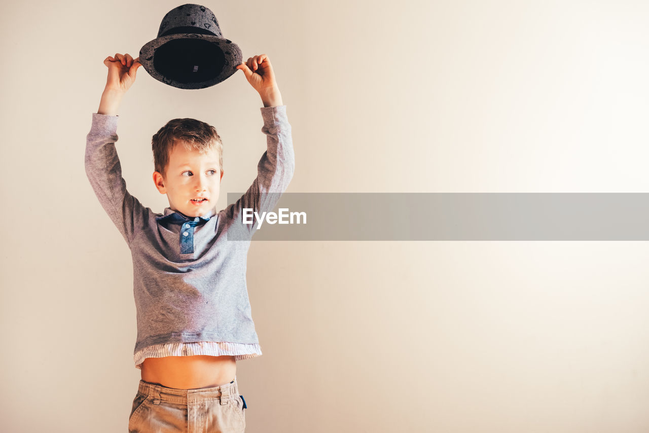 Boy holding hat against white wall