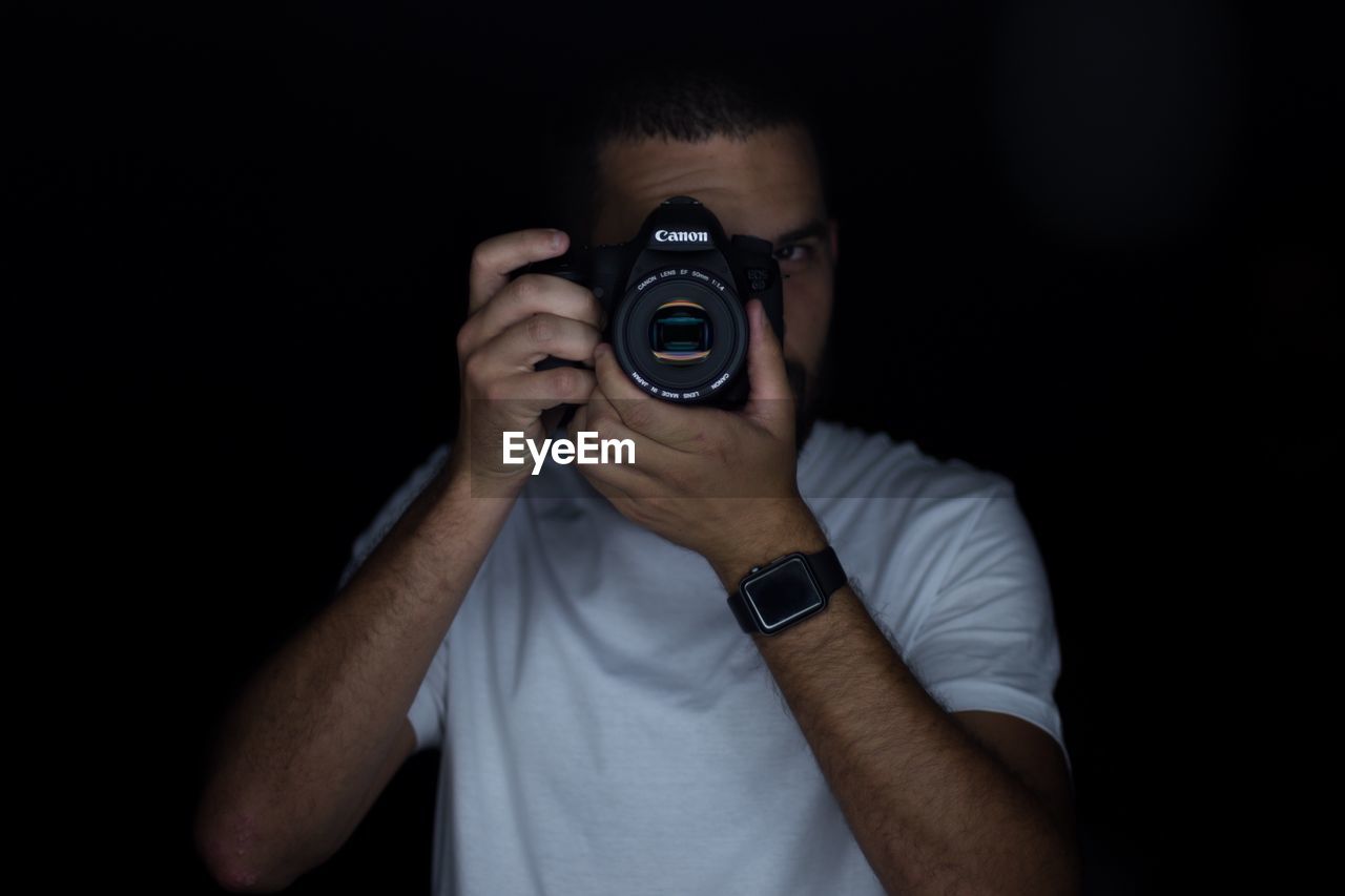 MIDSECTION OF MAN HOLDING CAMERA AT HOME