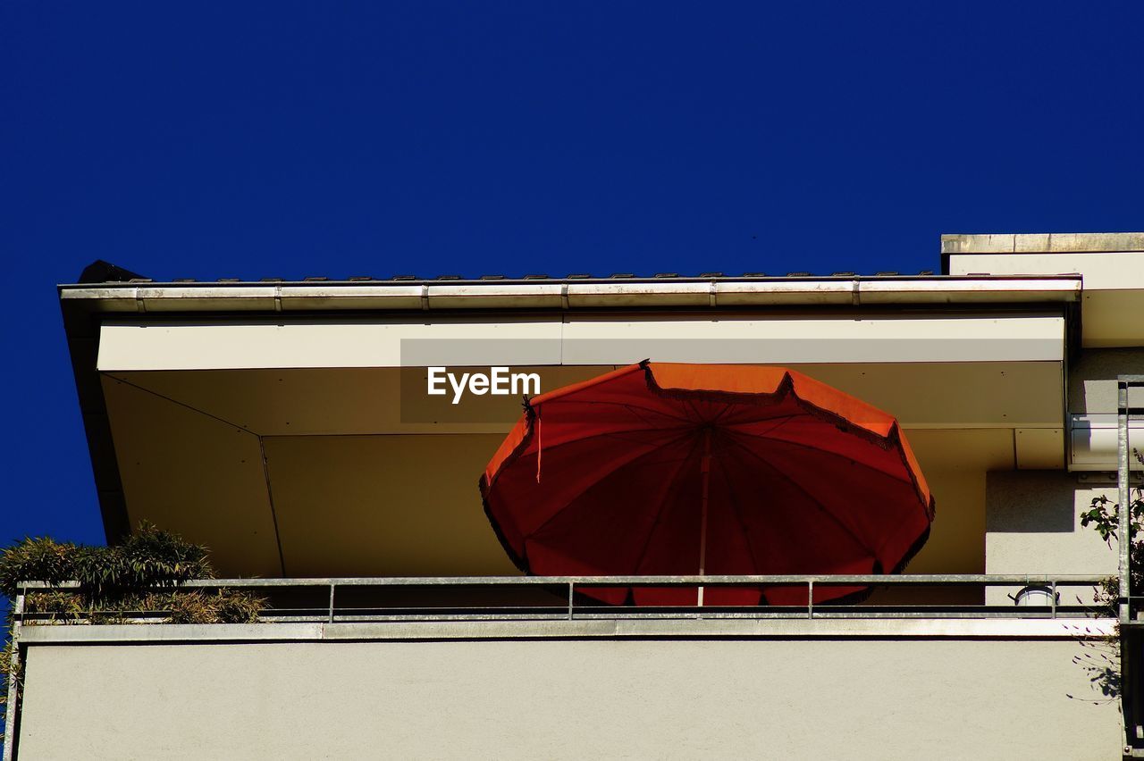 Low angle view of balcony with red umbrella against blue sky