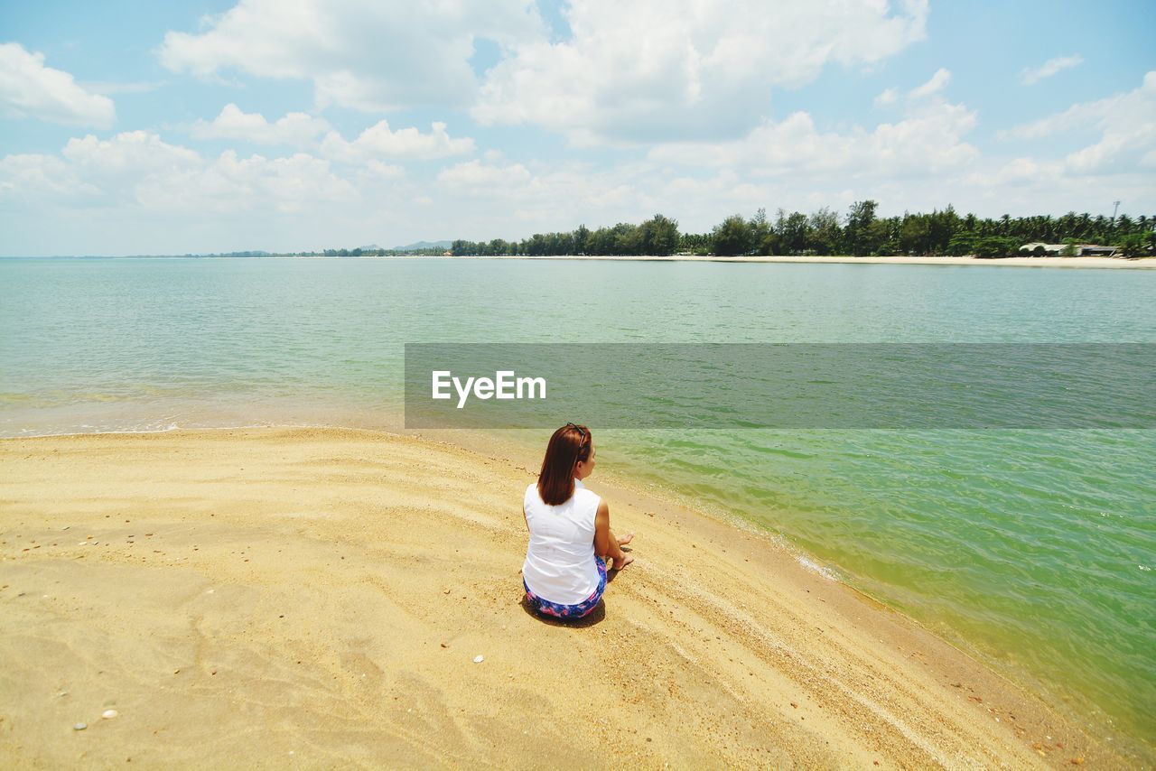 Rear view of woman sitting on shore at beach