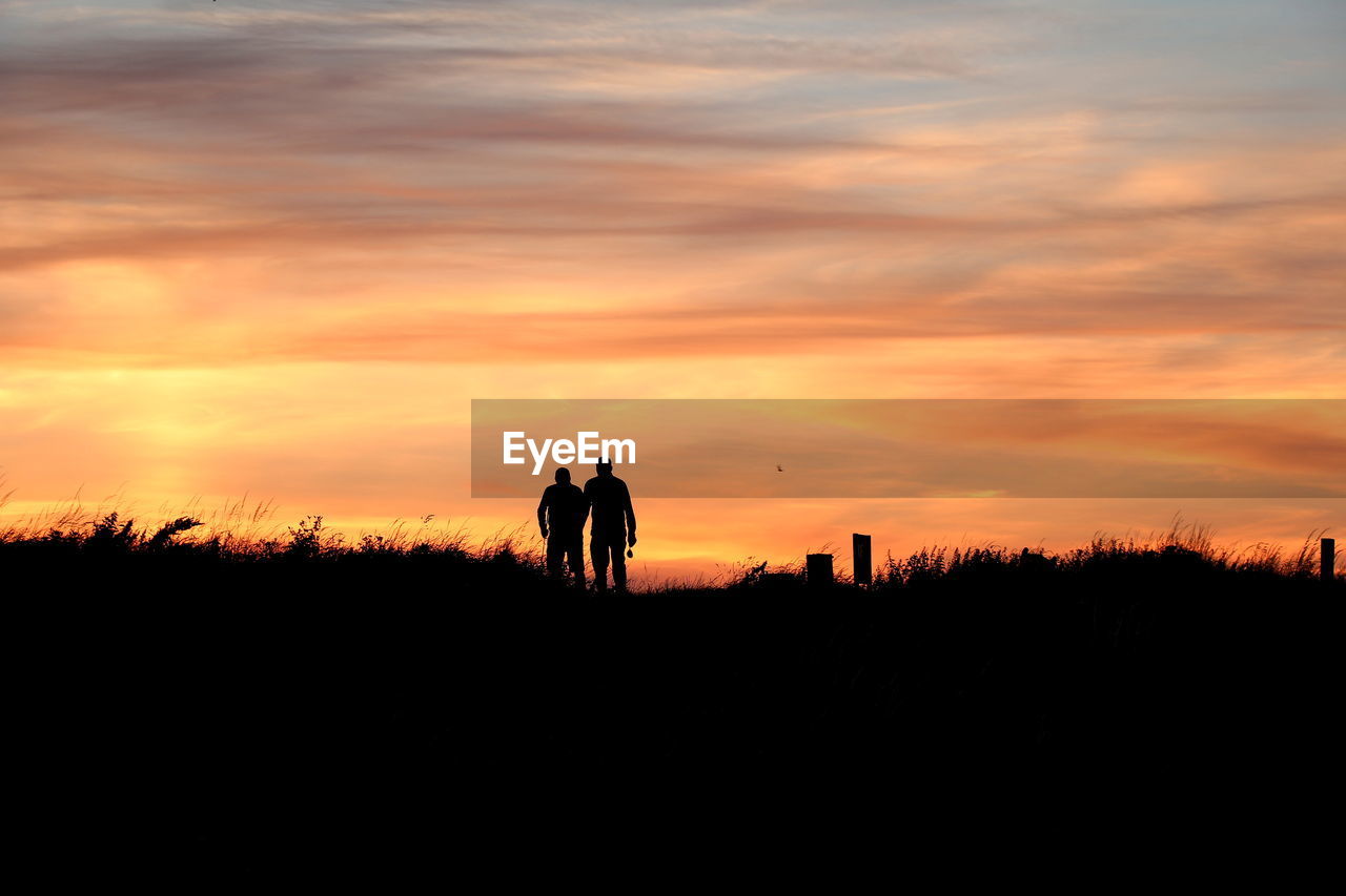 Silhouette men on field against sky during sunset