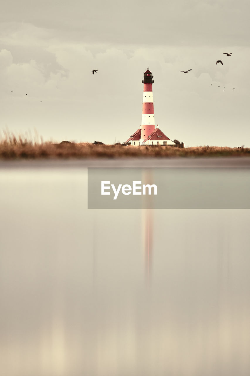 lighthouse by sea against sky at sunset