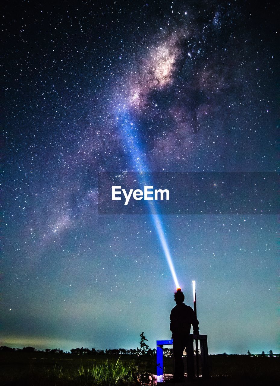 Rear view of man standing on land against sky at night