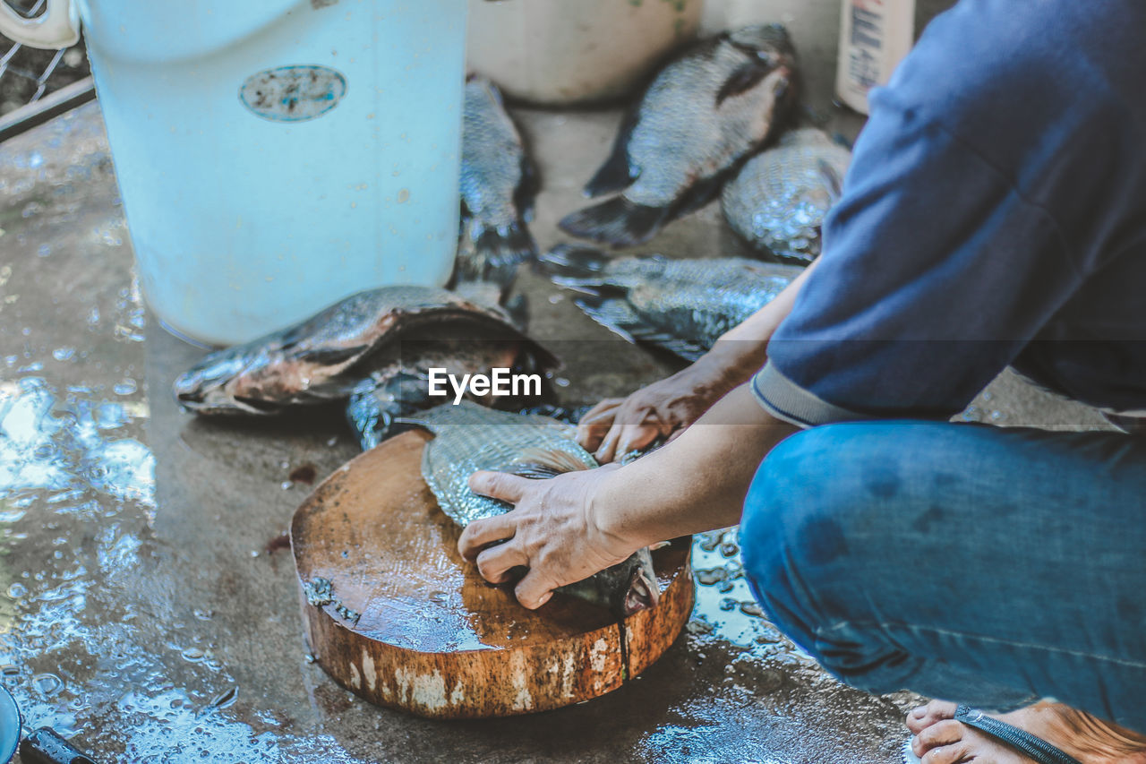 Midsection of man cutting fish in market