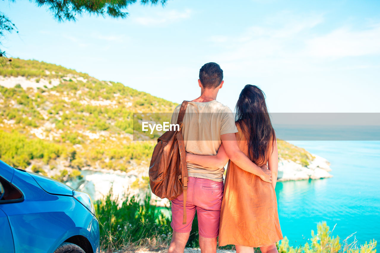 Rear view of friends standing on shore against sky