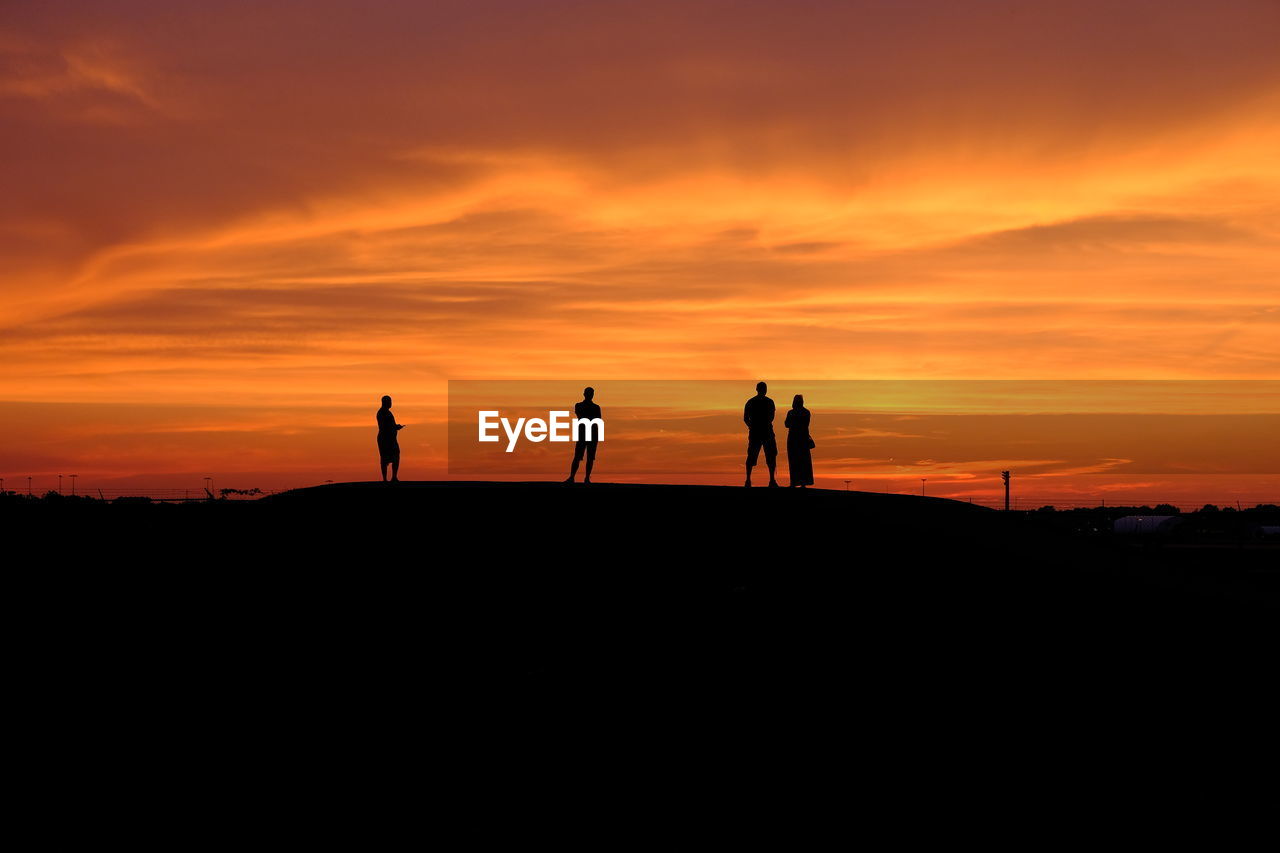 Silhouette people standing on field against cloudy sky during sunset