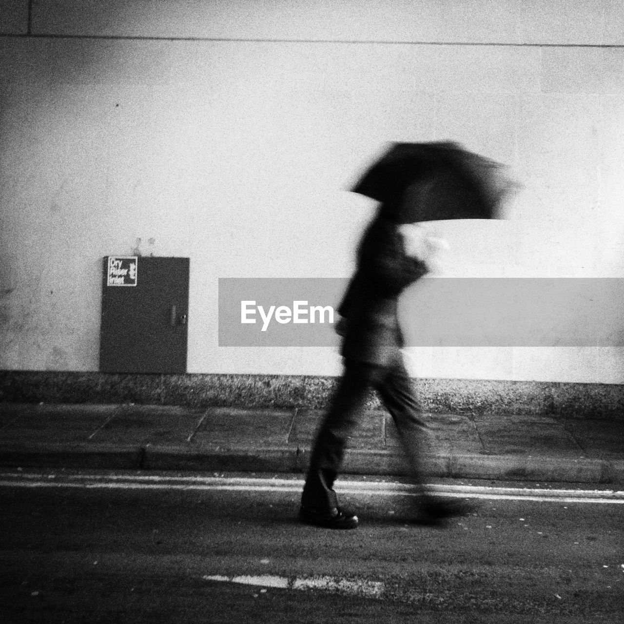 Side view of blurred man walking with umbrella along wall