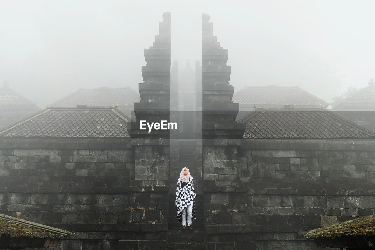 Woman standing against temple during foggy weather