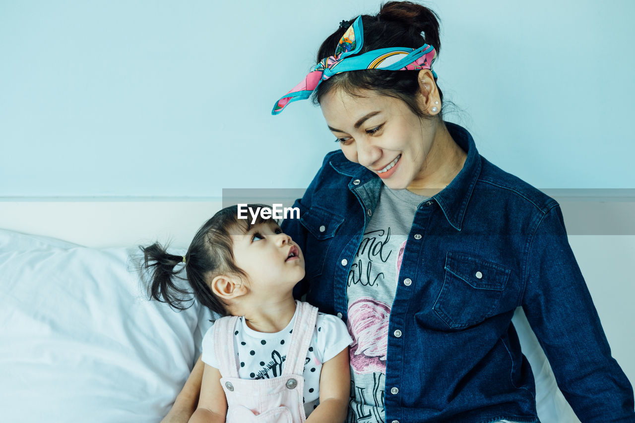 Smiling woman with daughter sitting on bed at home