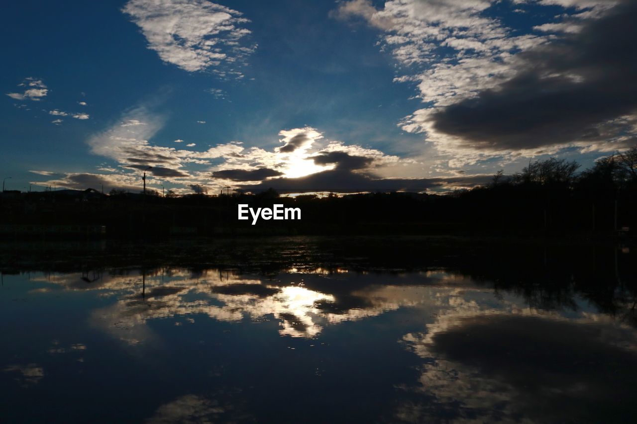 REFLECTION OF SILHOUETTE TREES IN LAKE AGAINST SKY DURING SUNSET