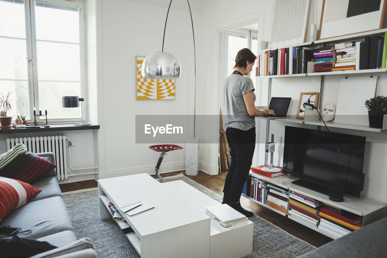 Rear view of industrial designer using laptop at shelf in home