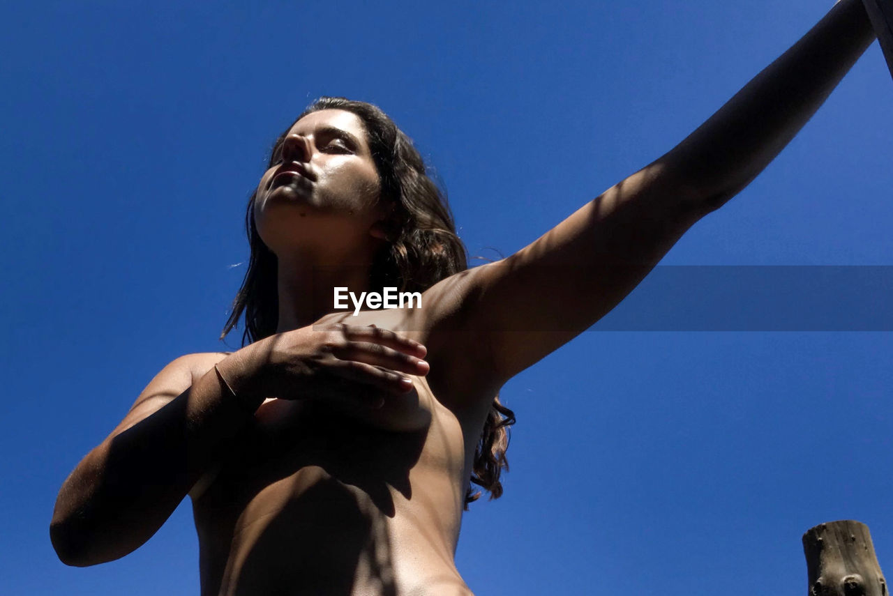 Low angle view of shirtless woman standing against blue sky