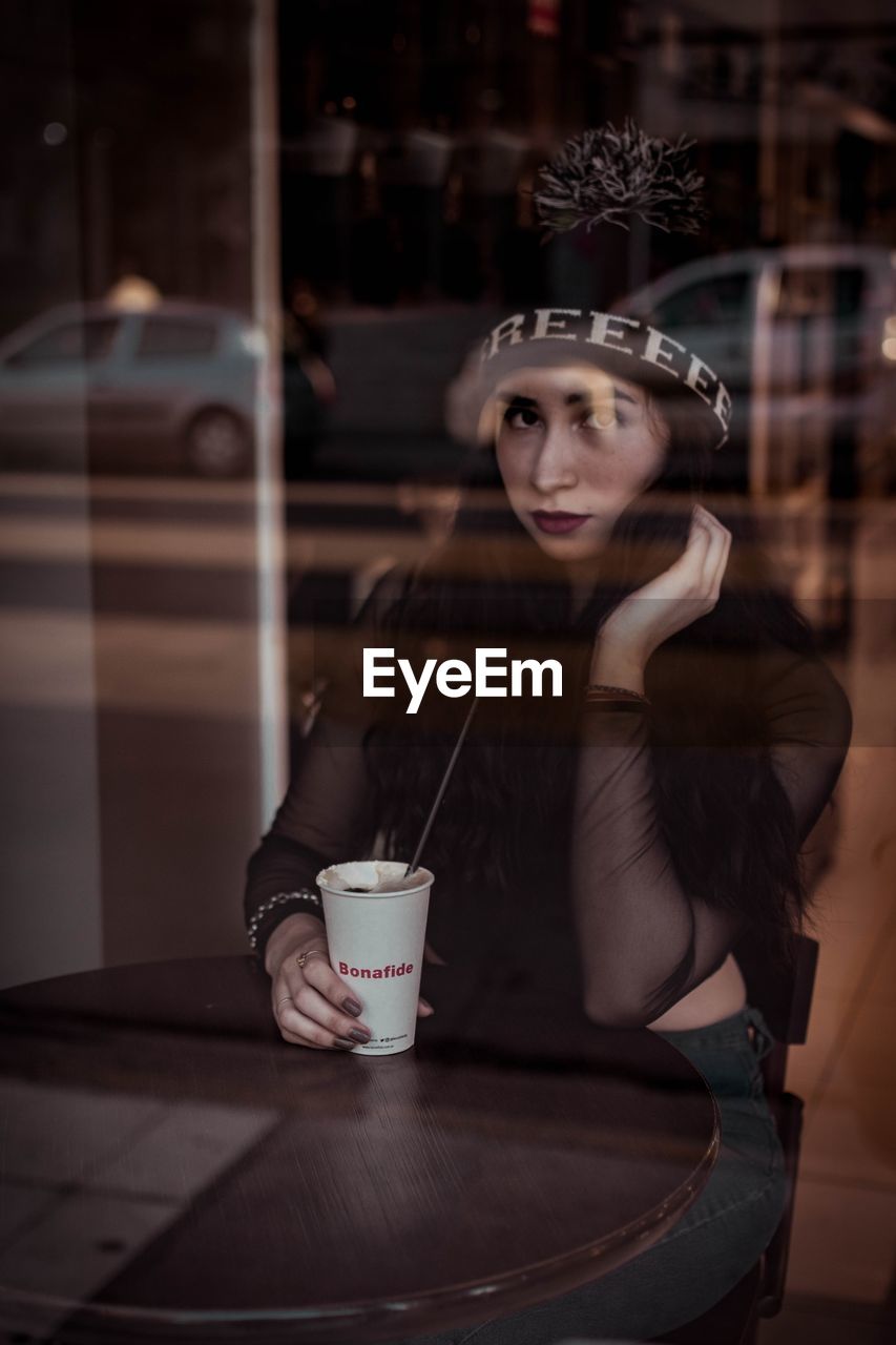 PORTRAIT OF WOMAN SITTING WITH DRINK