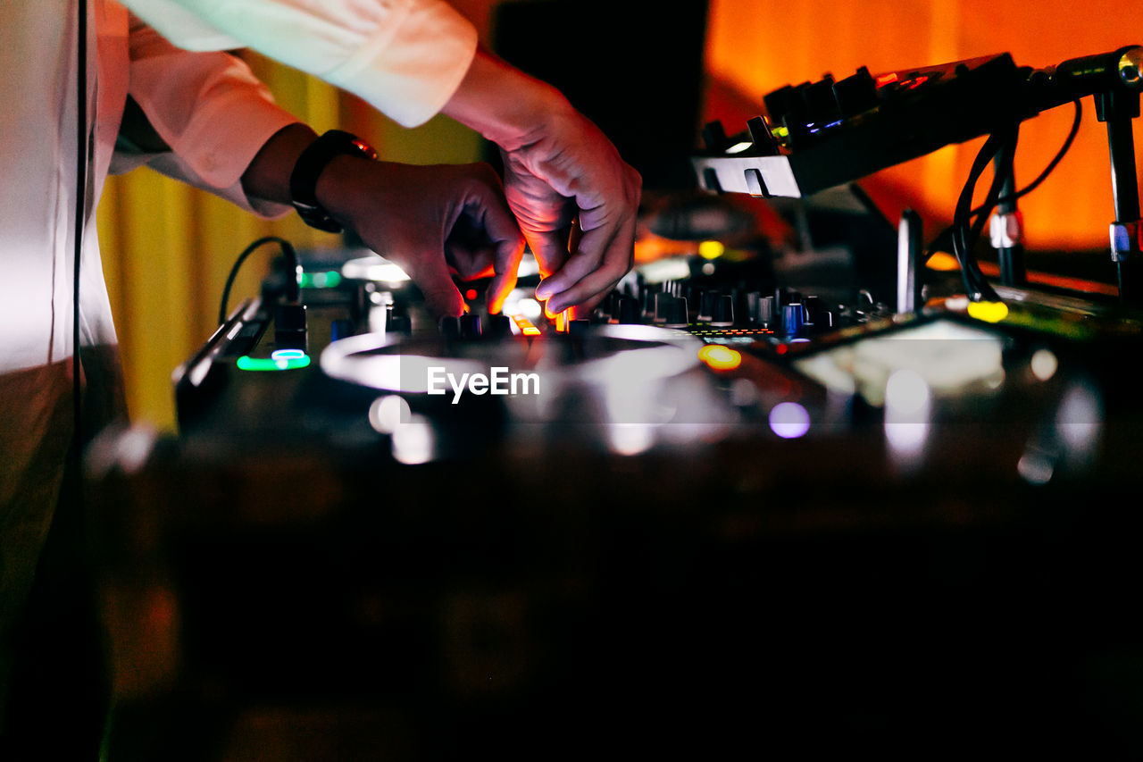 Dj is playing music. you can see his hands mixing music with his dj a party in the background.