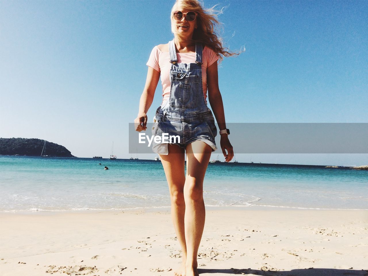 Full length of young woman walking at beach against clear sky