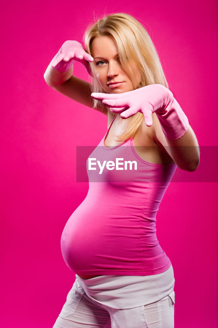 Pregnant woman standing against pink background