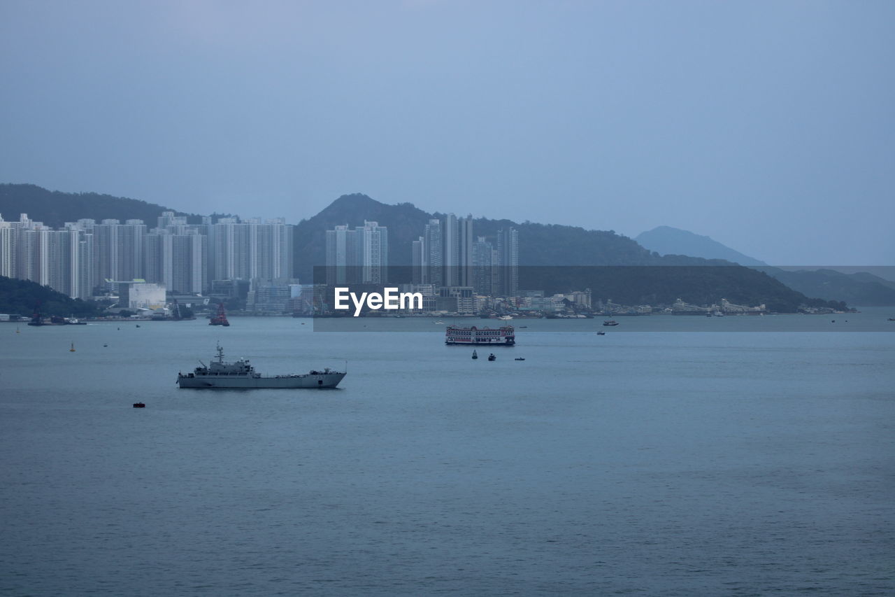 Boats in sea by buildings at city against clear sky