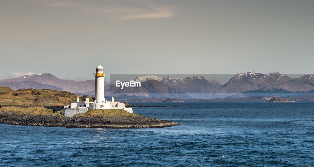 Eilean musdile lighthouse in scotland by sea and mountain against warm evening sky