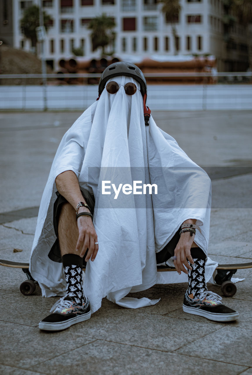 Rear view of a ghost costume doing skateboarding on street in city