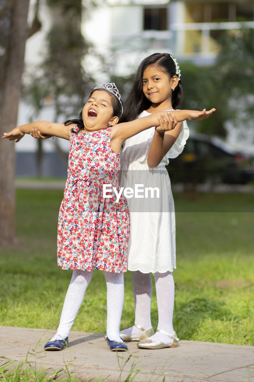 Portrait of girl standing by happy sister on footpath