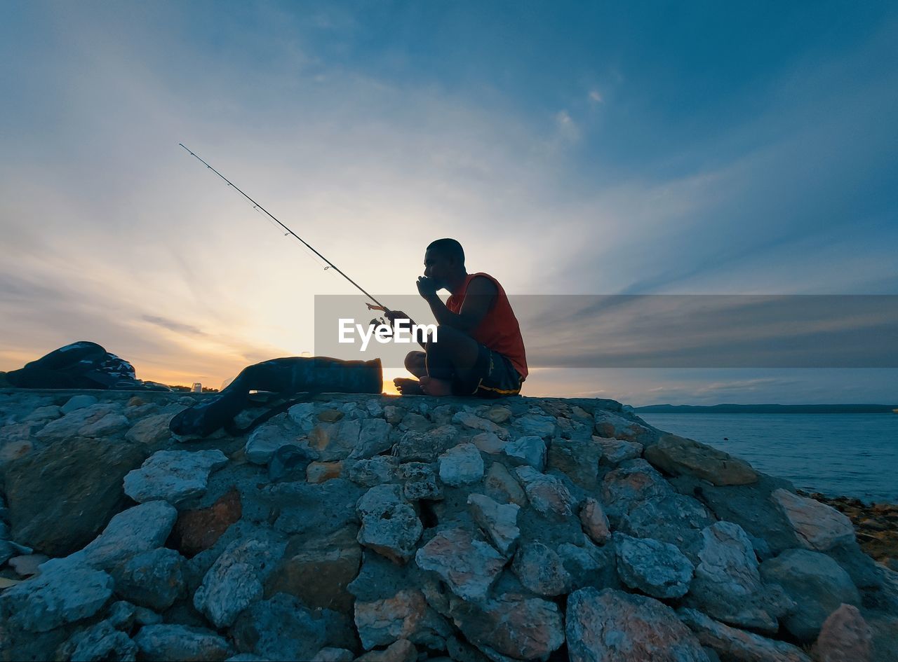 Rear view of man standing on rock at beach against sky