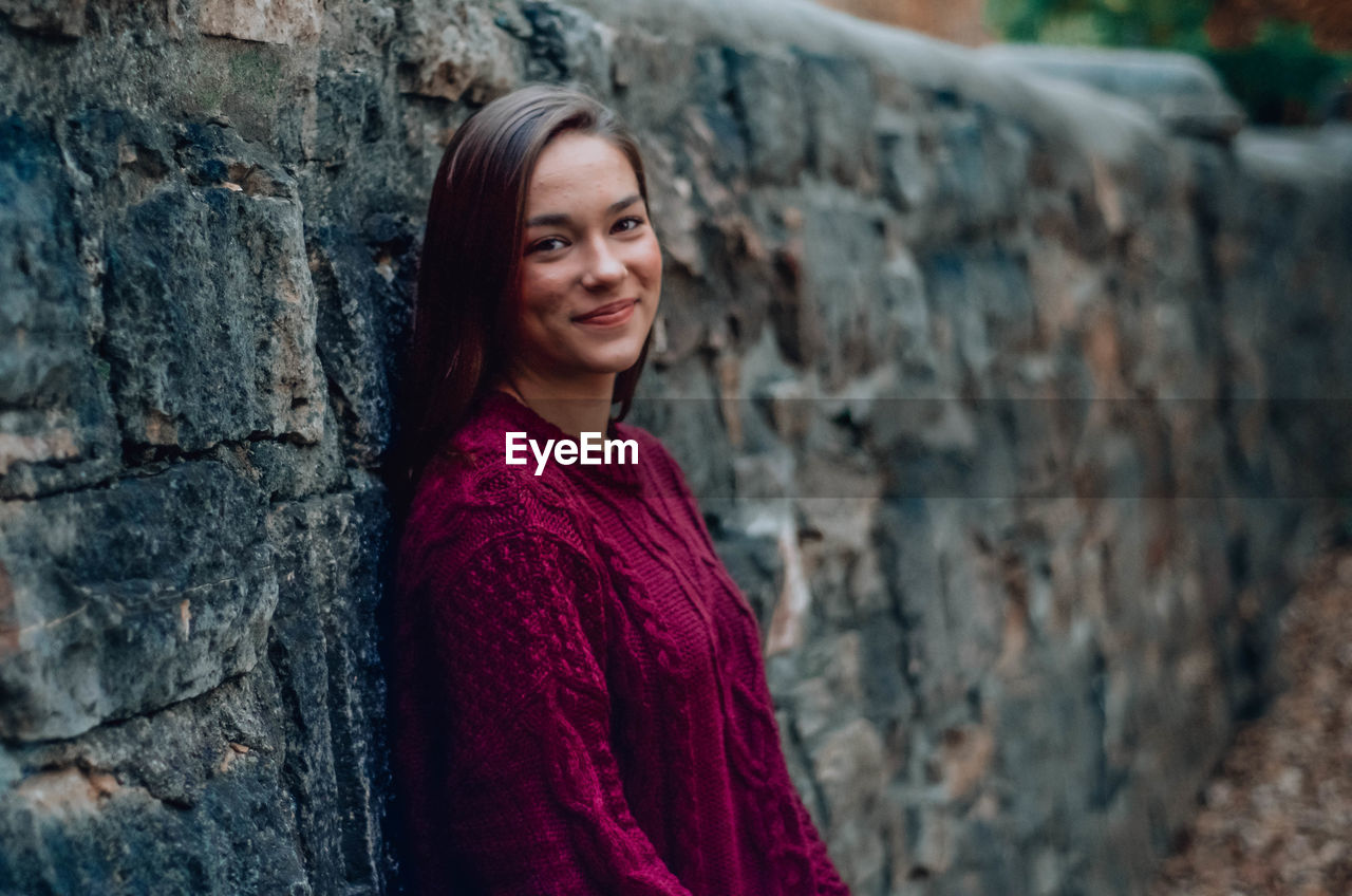 Portrait of smiling young woman standing by wall outdoors