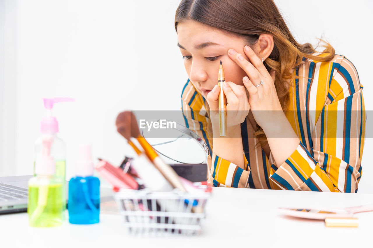 Young woman blogging while applying beauty product on table