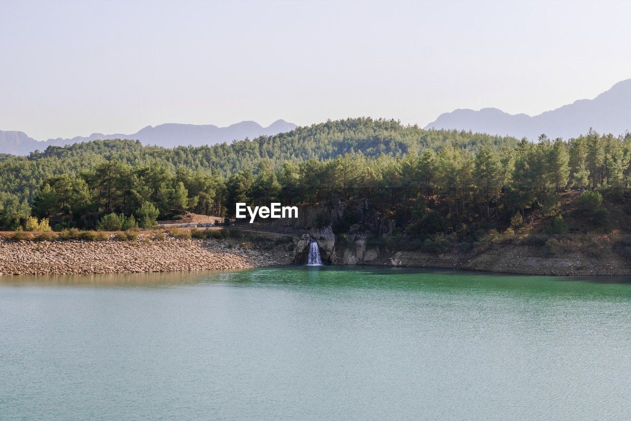 Tranquil forest lake with rocky waterfall and mountainous horizon